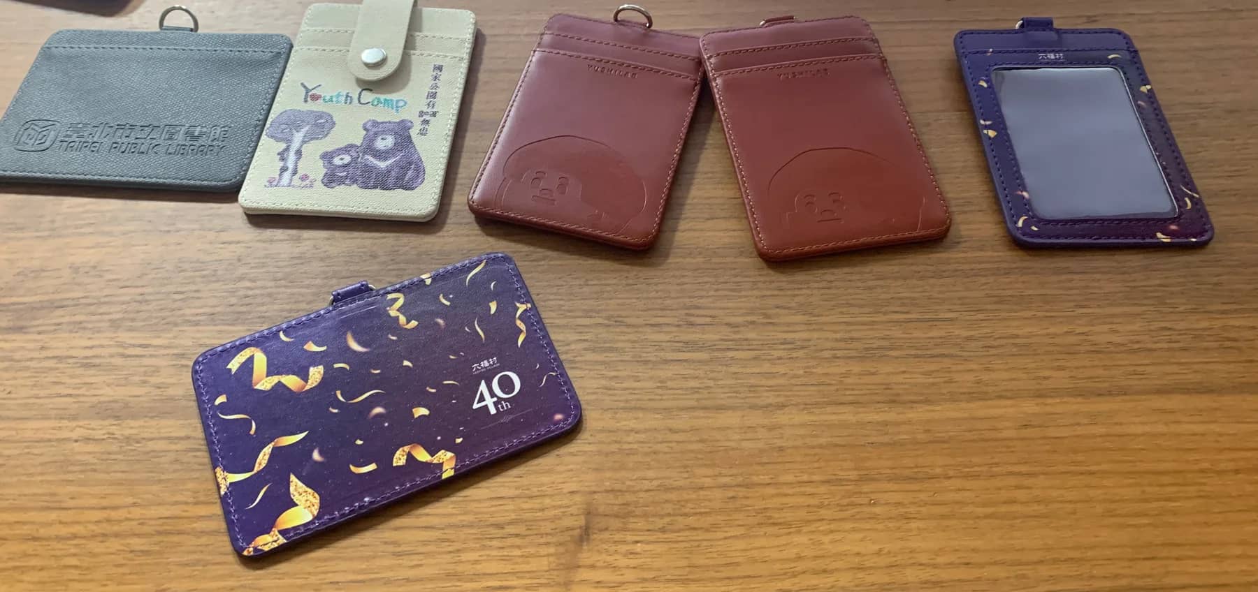 六件不同客戶的證件套成品同桌合影:壓印、彩印帆布、打凹皮款與滿版彩印